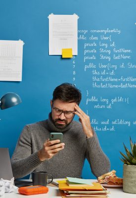 Frustrated depressed male freelancer cannot send message to client, looks sadly at smartphone, keeps hand on temple, suffers from headache, searches needed information, tired of doing remote work Frustrated depressed male freelancer cannot send message to client, looks sadly at smartphone, keeps hand on temple, suffers from headache, searches needed information, tired of doing remote work